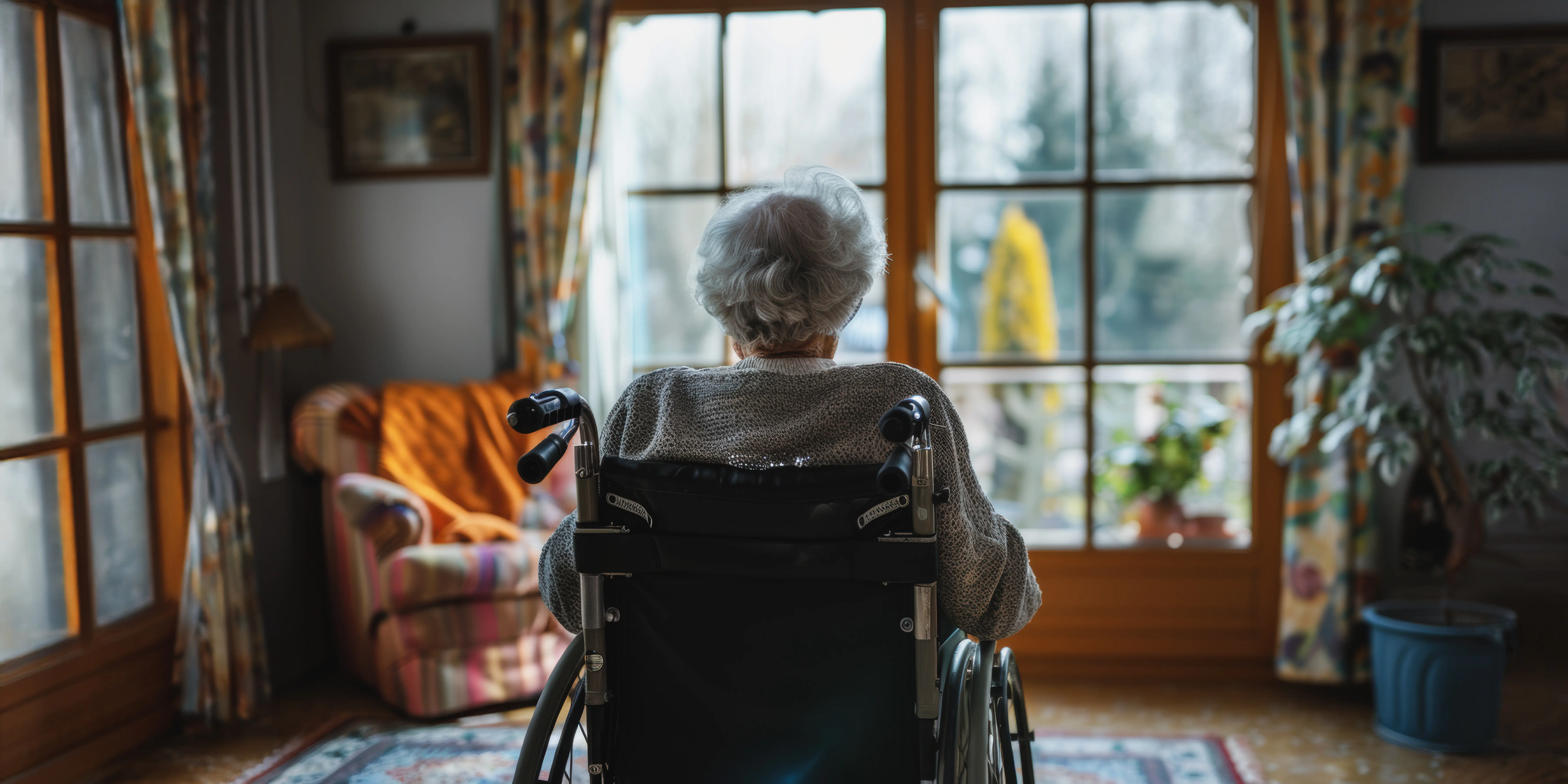 Ältere Frau im Rollstuhl schaut zu Hause aus dem Fenster.